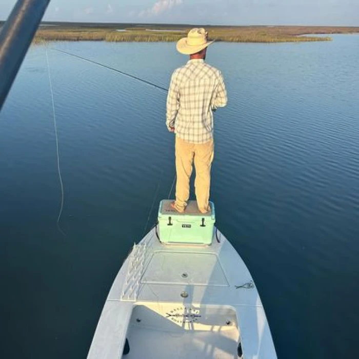 A person standing on the bow of a boat, fishing on calm waters.