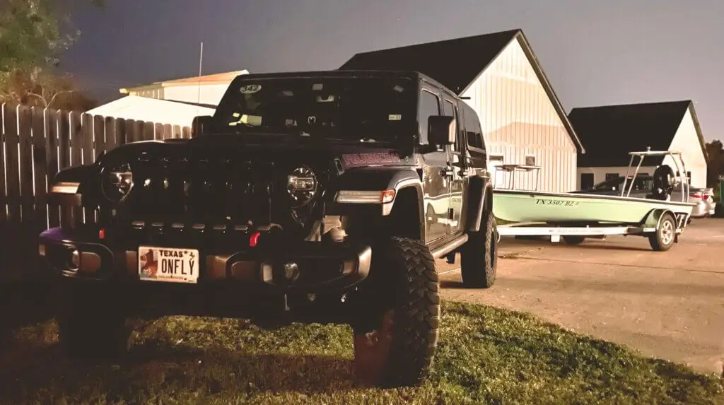 Black Jeep Rubicon with trailer and boat at night.